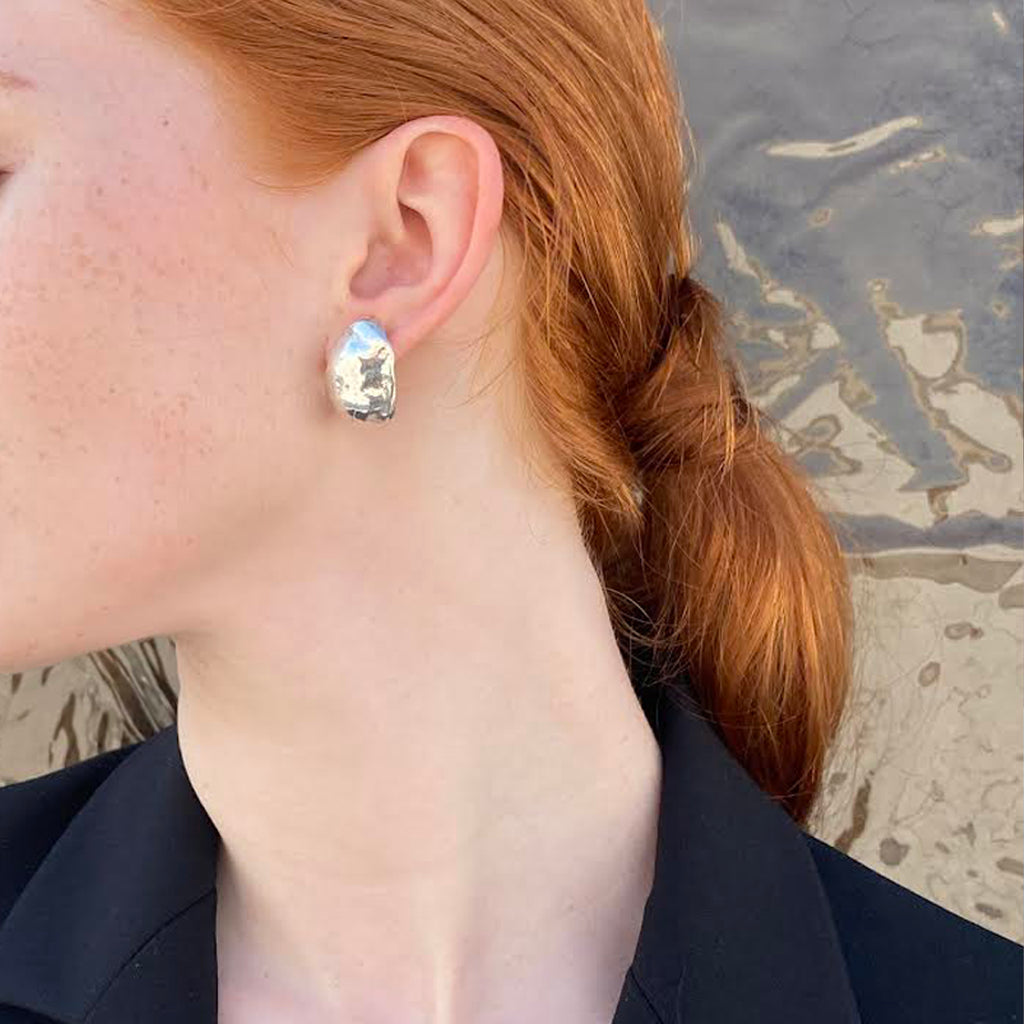 Woman wearing bold silver earrings with organic, sculptural shape inspired by Hawaiian Kukui nuts
